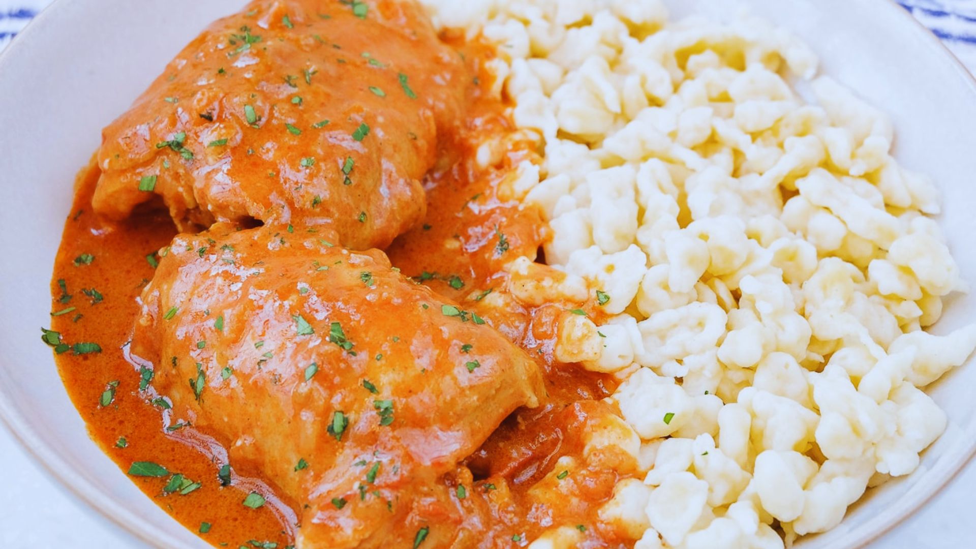A baked chicken and macaroni casserole topped with golden cheese and herbs, served in a white dish.