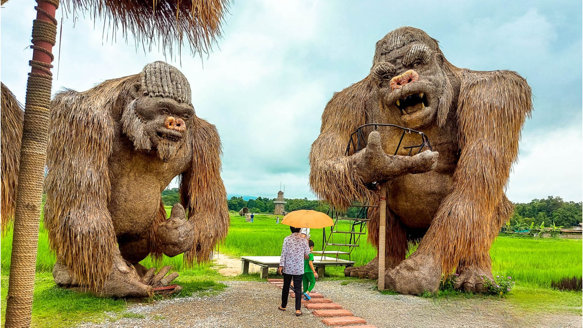 A man poses next to two enormous gorilla statues, highlighting their grandeur in a public space.