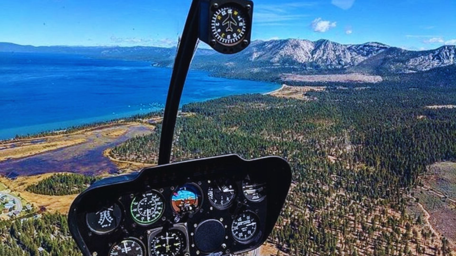 A helicopter soars over mountains, offering a scenic view of a tranquil lake below.
