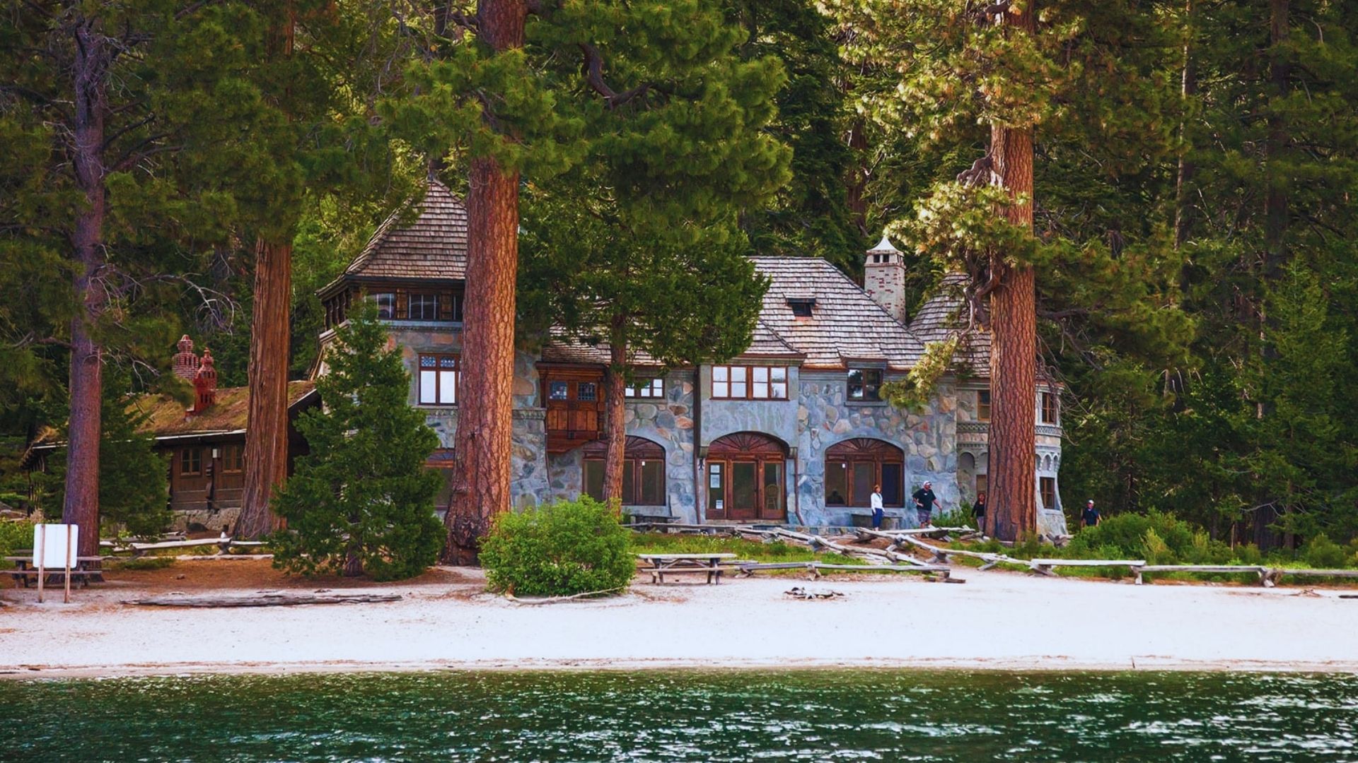 A large house situated on the edge of a serene lake, surrounded by lush greenery and reflecting in the water.