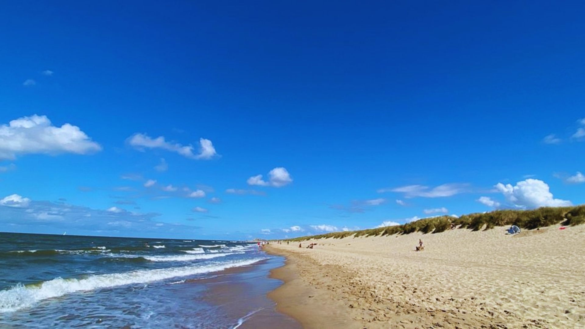 A sandy beach with gentle waves lapping at the shore under a clear blue sky.