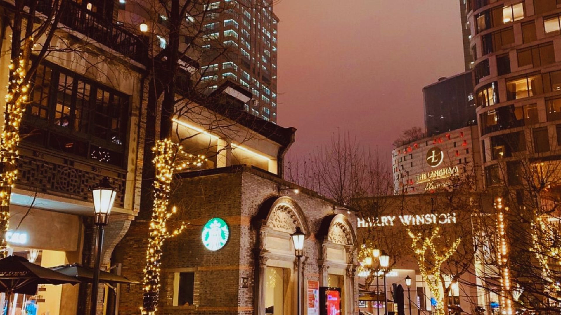 A city street illuminated by lights on buildings and trees, creating a vibrant evening atmosphere.