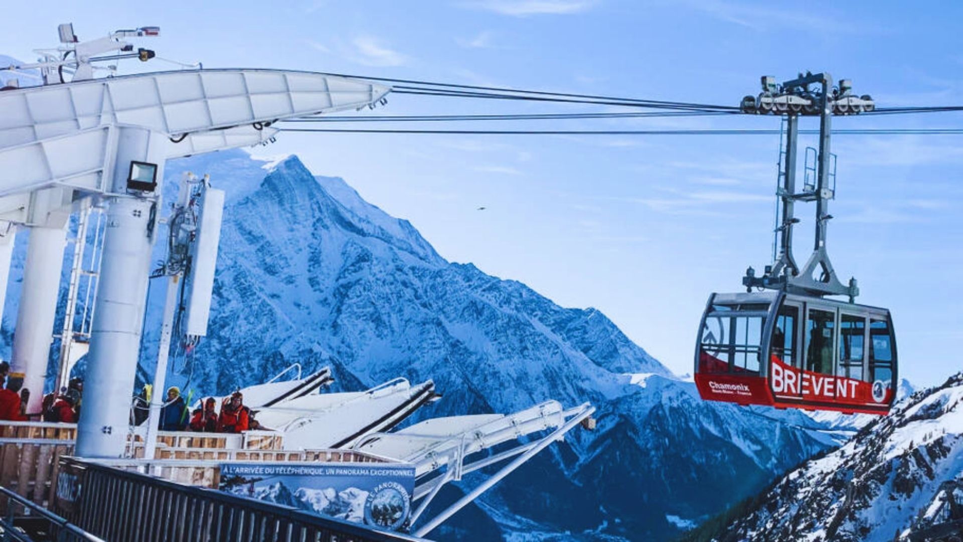 A cable car ascends a snowy mountain, with majestic snow-covered peaks visible in the background.