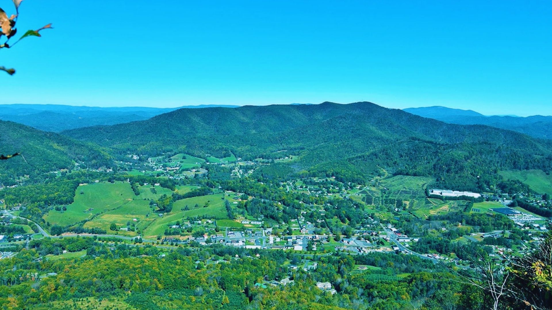 A panoramic view from a mountain peak, showcasing a lush valley below under a clear blue sky.