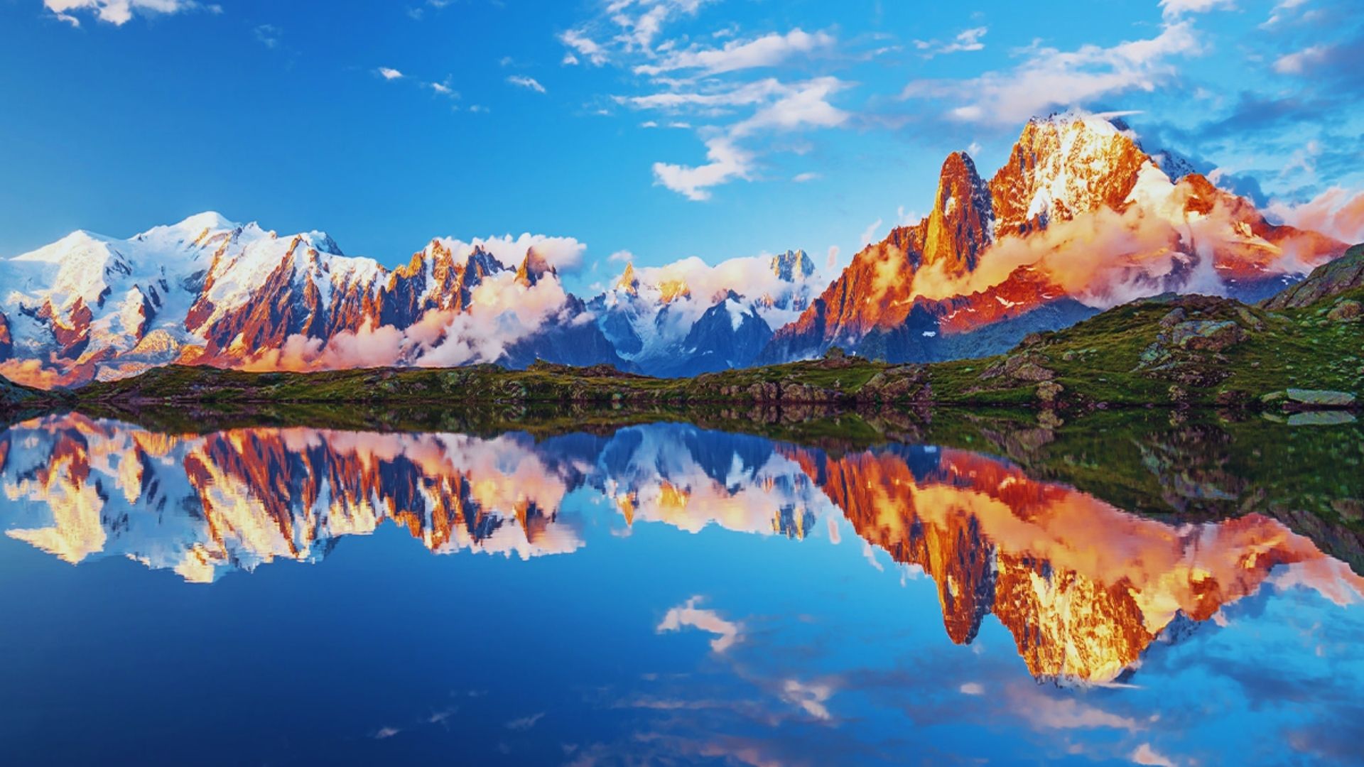 Serene sunset over mountains, their reflection shimmering in a tranquil lake below.