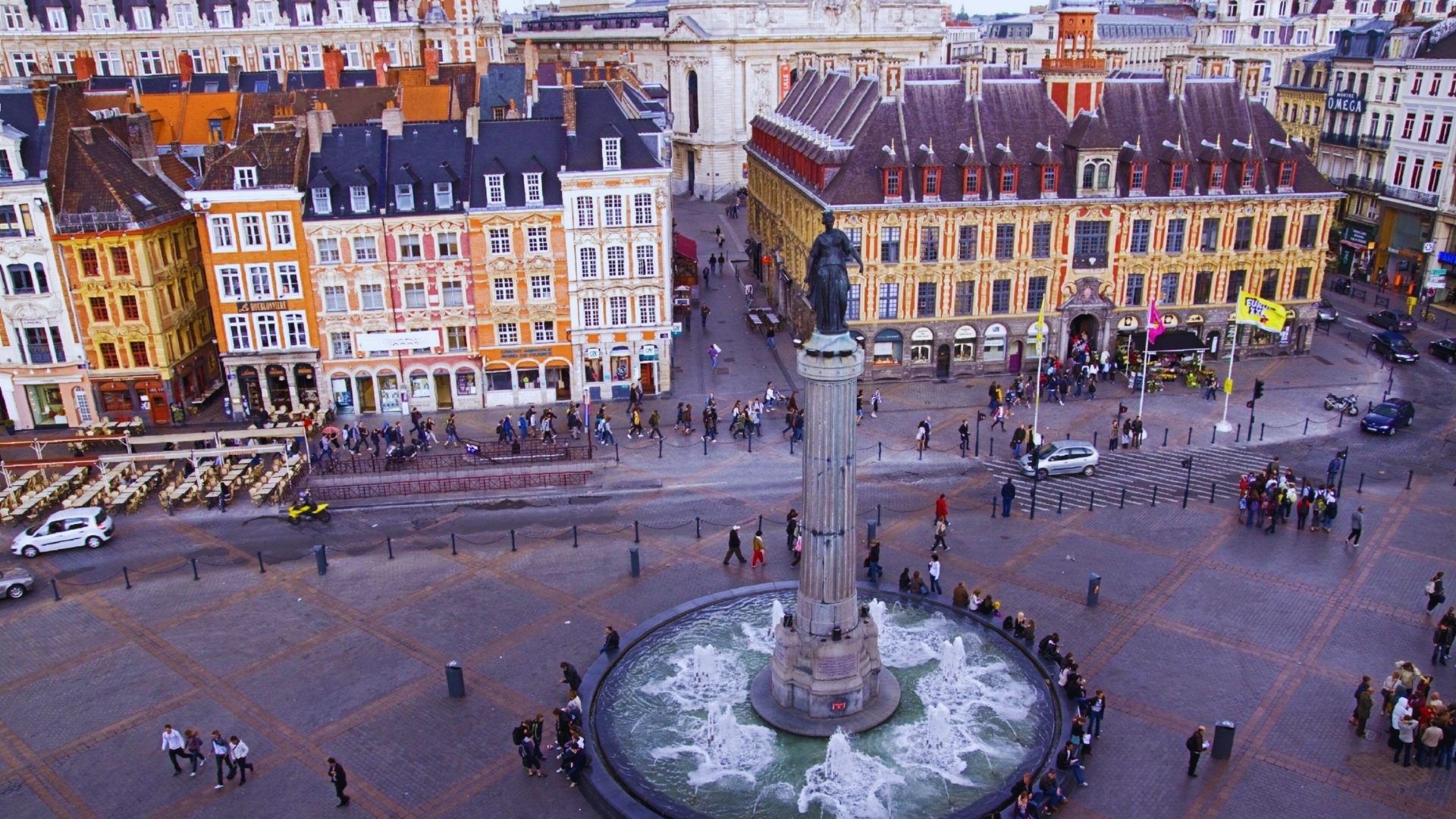 . A city square featuring a central fountain surrounded by buildings and greenery.