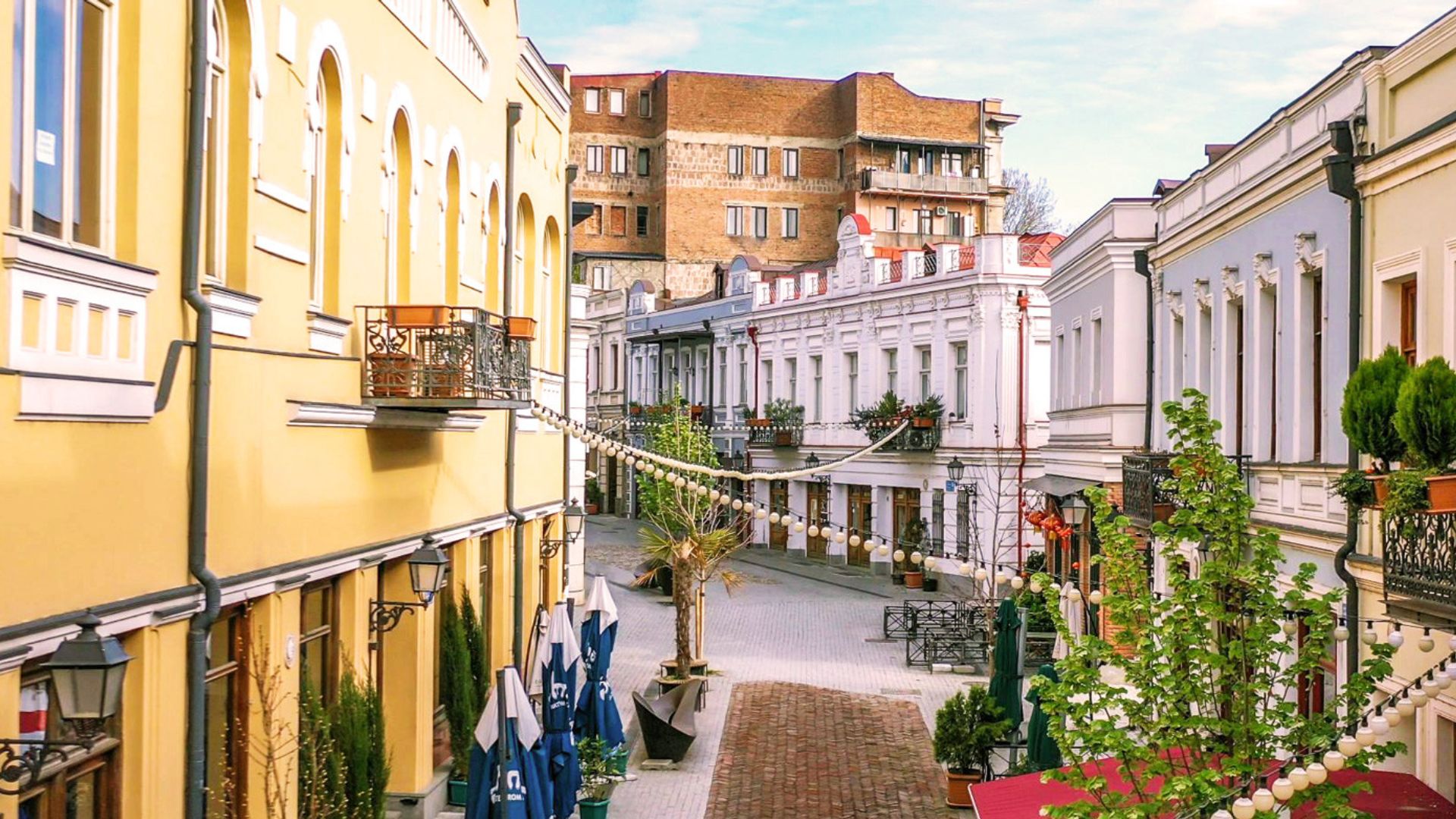 A narrow street lined with buildings, featuring a few pedestrians walking along the sidewalk.