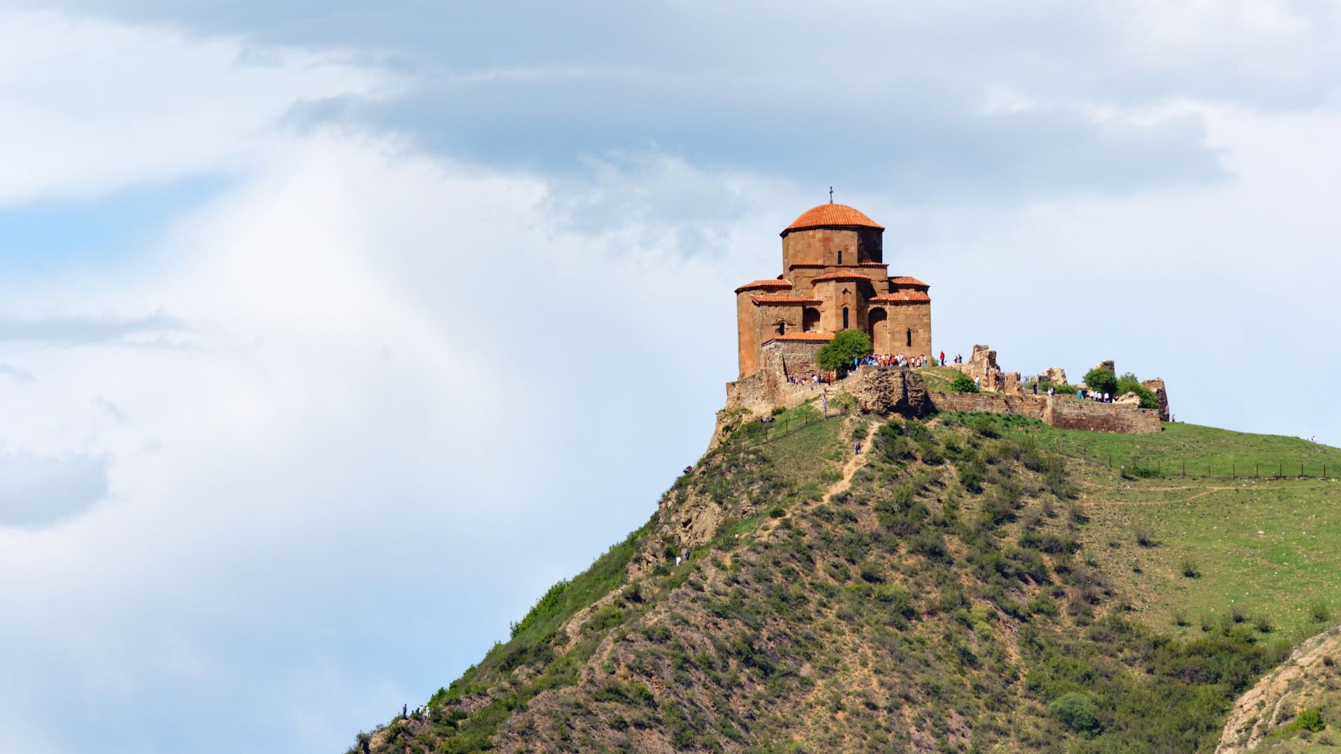 A scenic hill topped with a historic castle, surrounded by lush greenery and a clear blue sky.