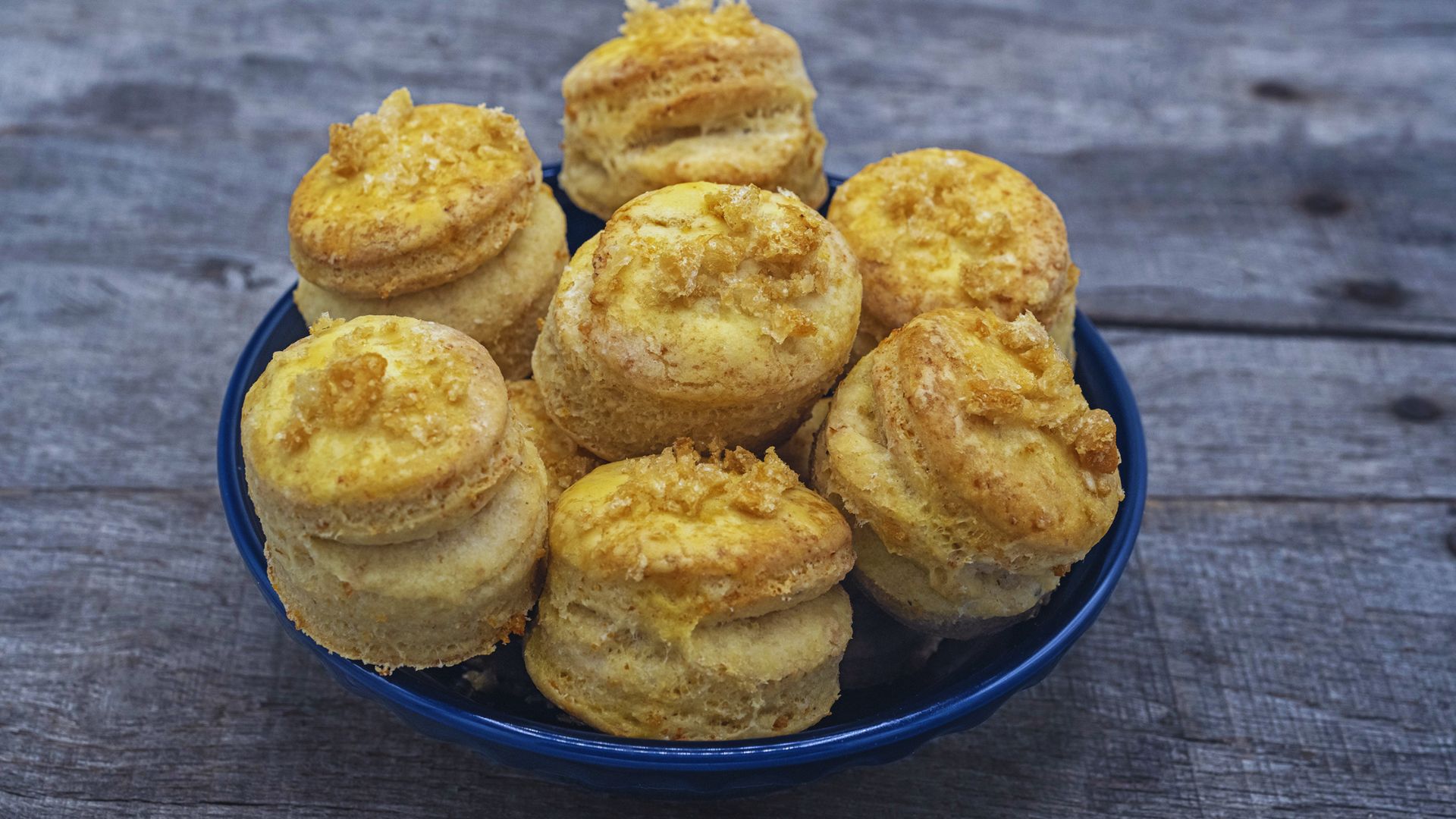 A bowl of freshly baked biscuits placed on a rustic wooden table.