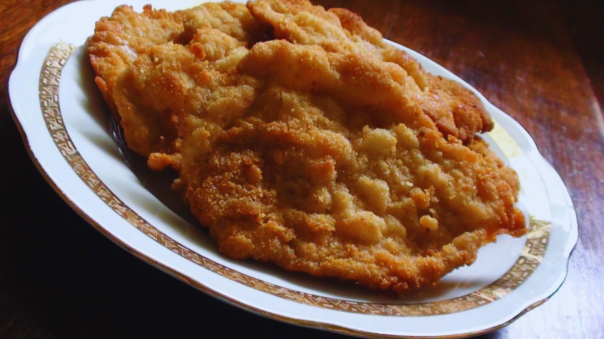 A plate of golden fried chicken served on a wooden table, garnished with herbs.