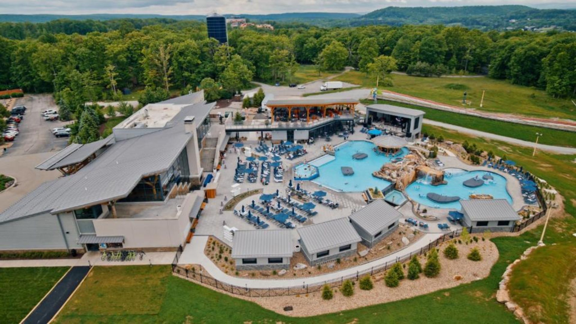 A hilltop resort featuring a swimming pool and expansive green lawn, surrounded by scenic views.
