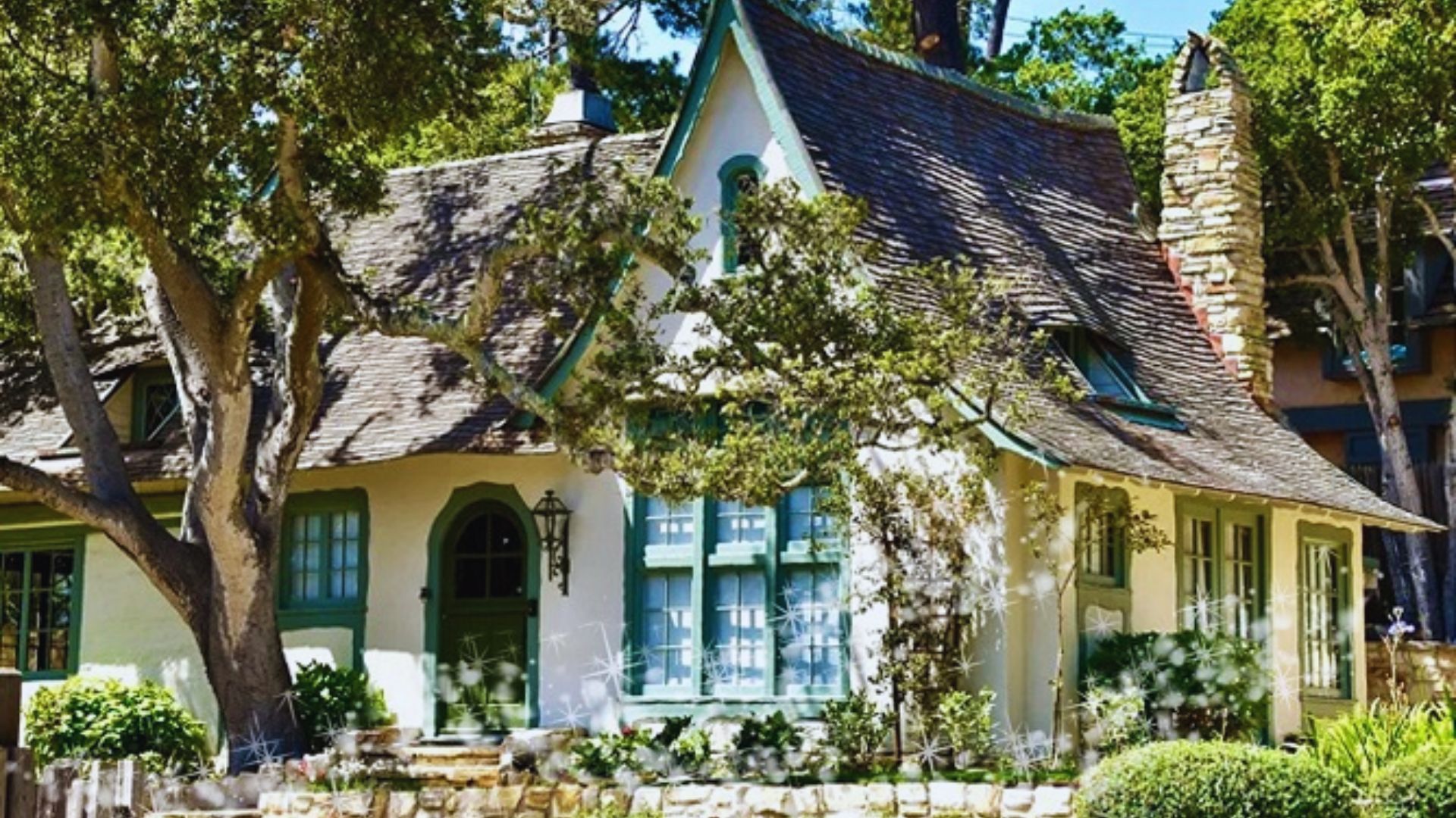 Charming fairytale cottage with green accents, steep roof, and stone chimney nestled among lush trees. Sunlight enhances the whimsical, cozy ambiance.