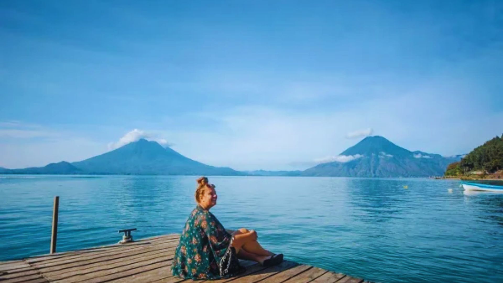 A woman sits on a dock, gazing thoughtfully at the calm water below.