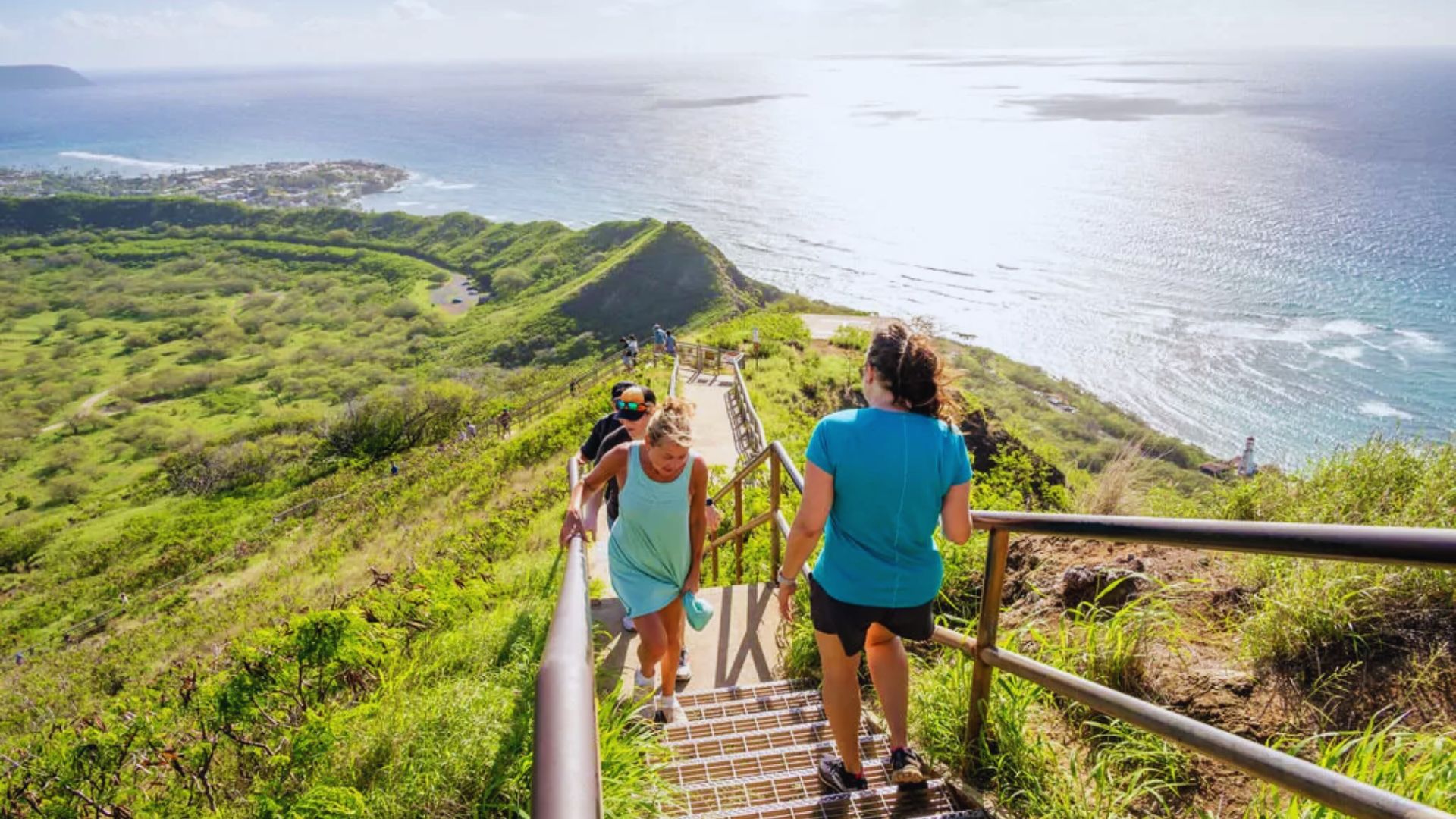A group of people ascending stairs leading to the summit of a mountain, surrounded by scenic views.