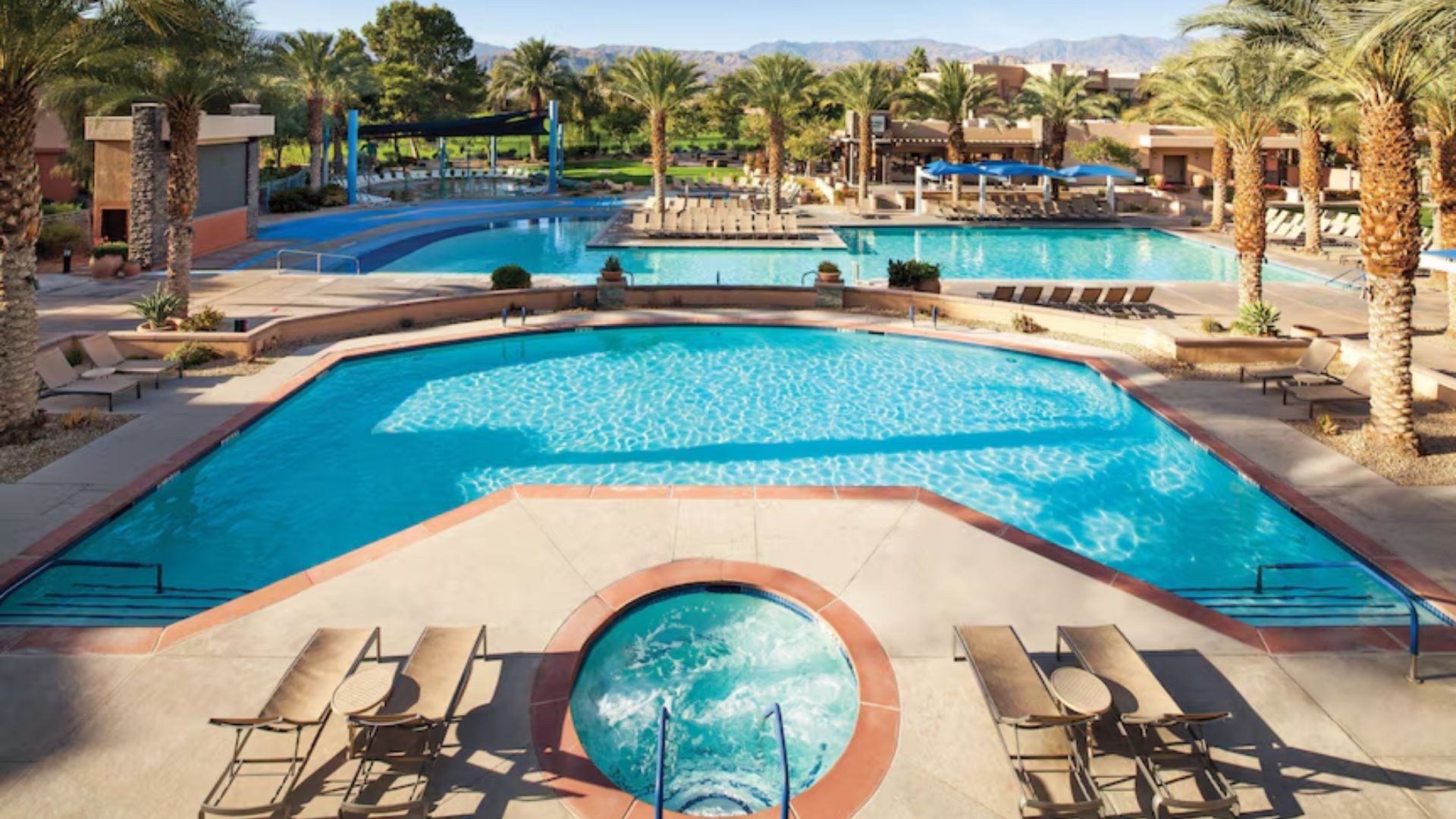 A vibrant resort pool in Las Vegas, surrounded by palm trees and lounge chairs under a clear blue sky.