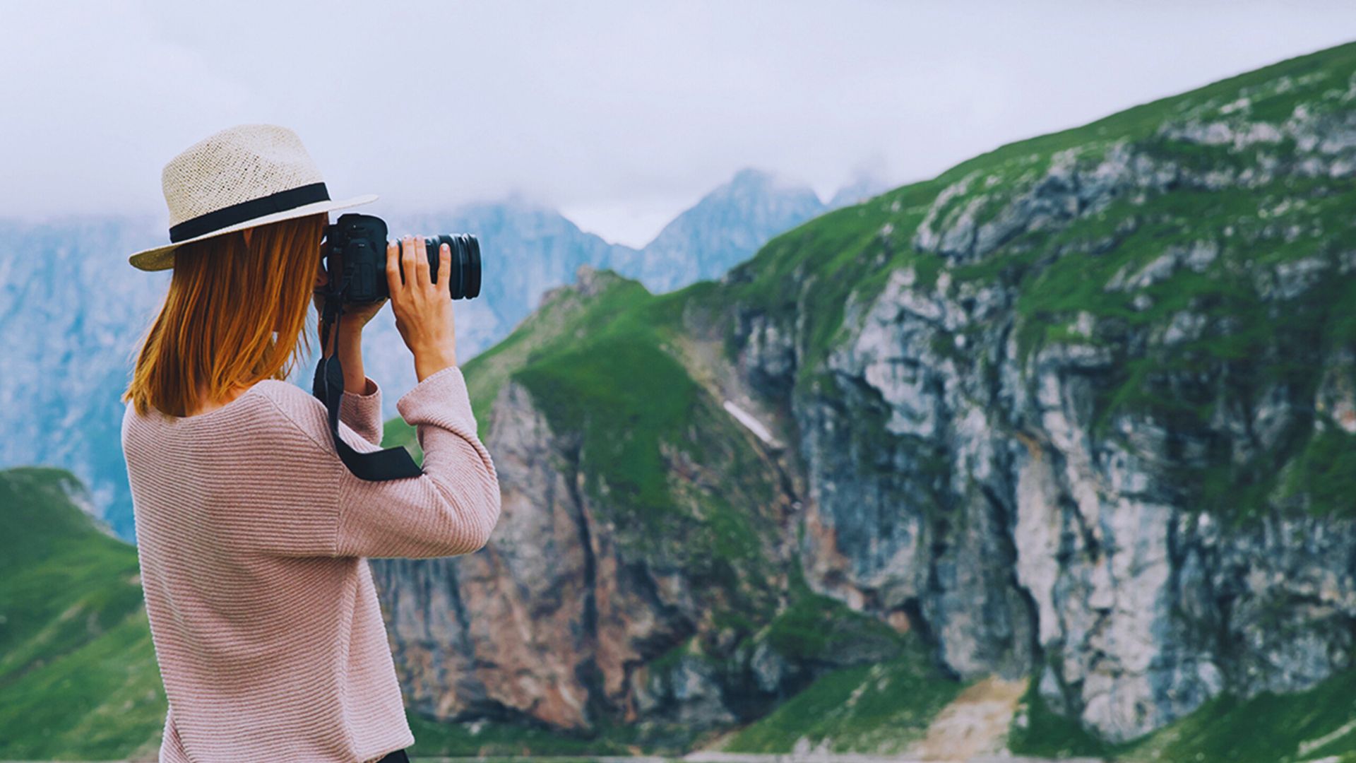 Woman photographing mountains with a camera, capturing the scenic landscape in the background.