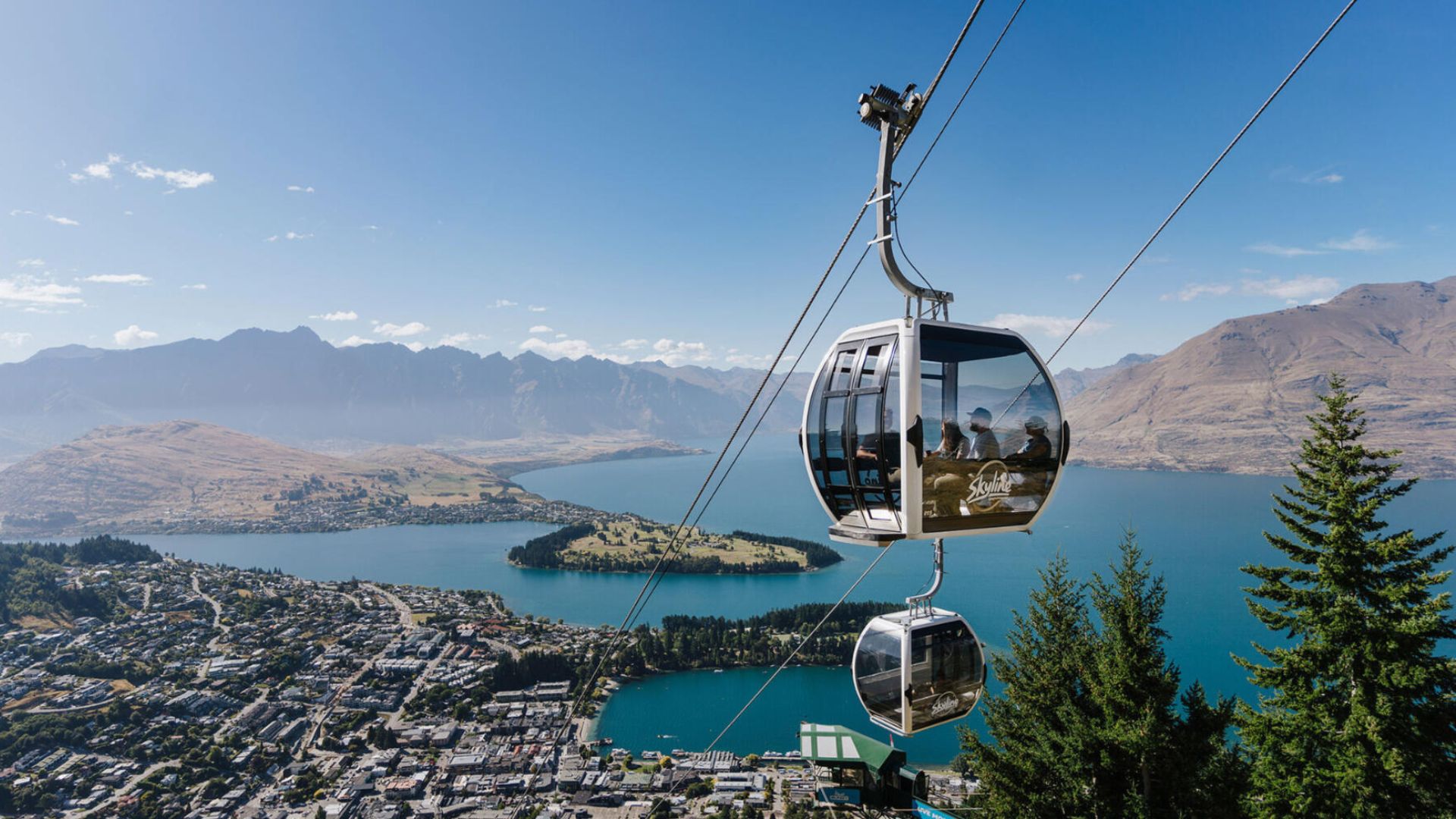 A scenic cable car glides over Queenstown, New Zealand, offering stunning views of the surrounding mountains and lake.