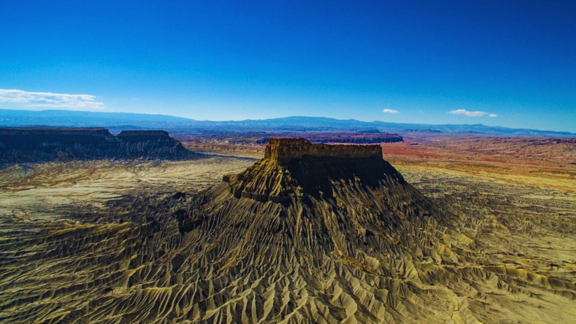 Aerial view of a vast desert landscape featuring rugged mountains under a clear blue sky.