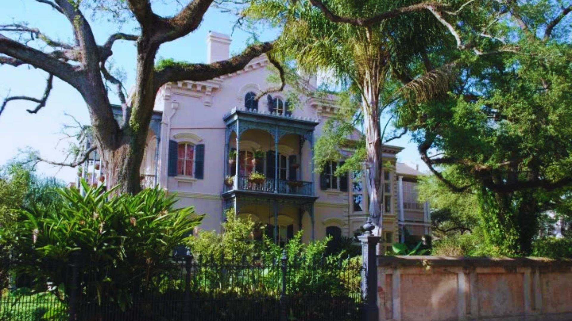 A spacious pink house with a white fence and green trees, creating a charming residential scene.