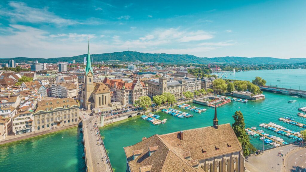A vibrant scene of Zurich, Switzerland, highlighting its stunning lake and historic buildings with a backdrop of mountains.