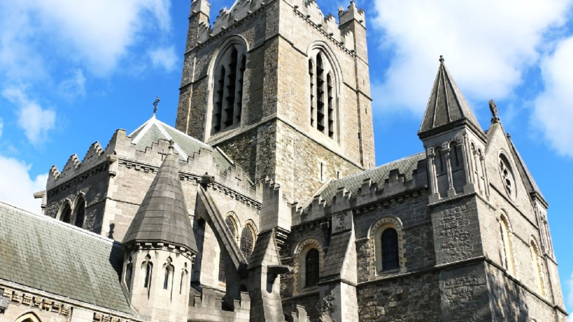 A large stone church featuring a tall tower with a clock, showcasing classic architectural design against a clear sky.