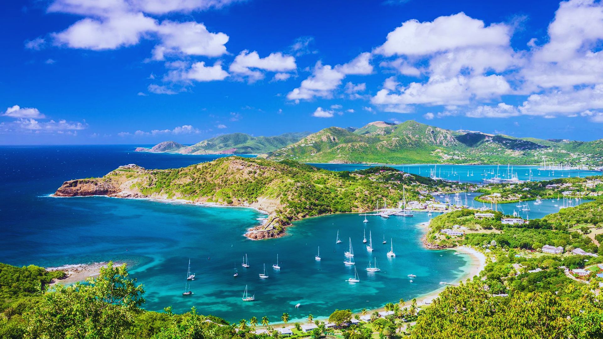 Vibrant coastal landscape with turquoise waters, sailboats, and lush green hills under a bright blue sky with scattered white clouds. Serene and inviting.