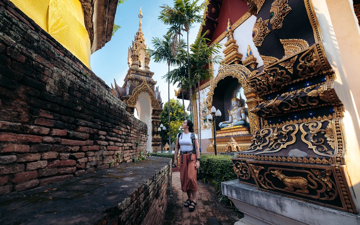 A woman walking through a traditional Thai temple, surrounded by ornate architecture and lush greenery.