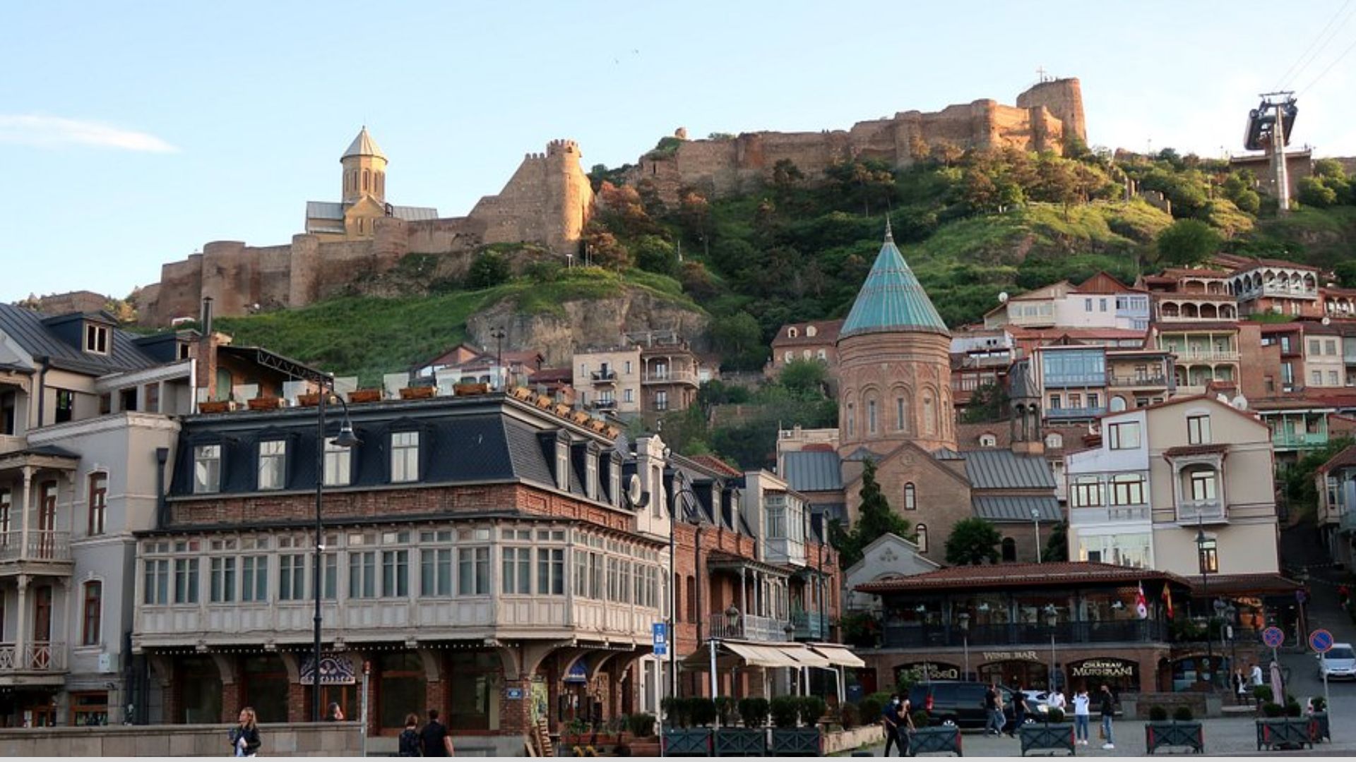 A panoramic view of a city with a prominent castle perched atop a hill, overlooking the urban landscape below.