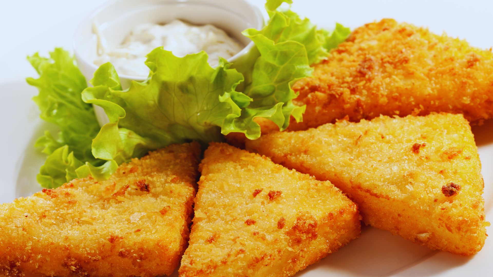 Fried fish cakes served on a bed of lettuce with a small bowl of dip on the side.