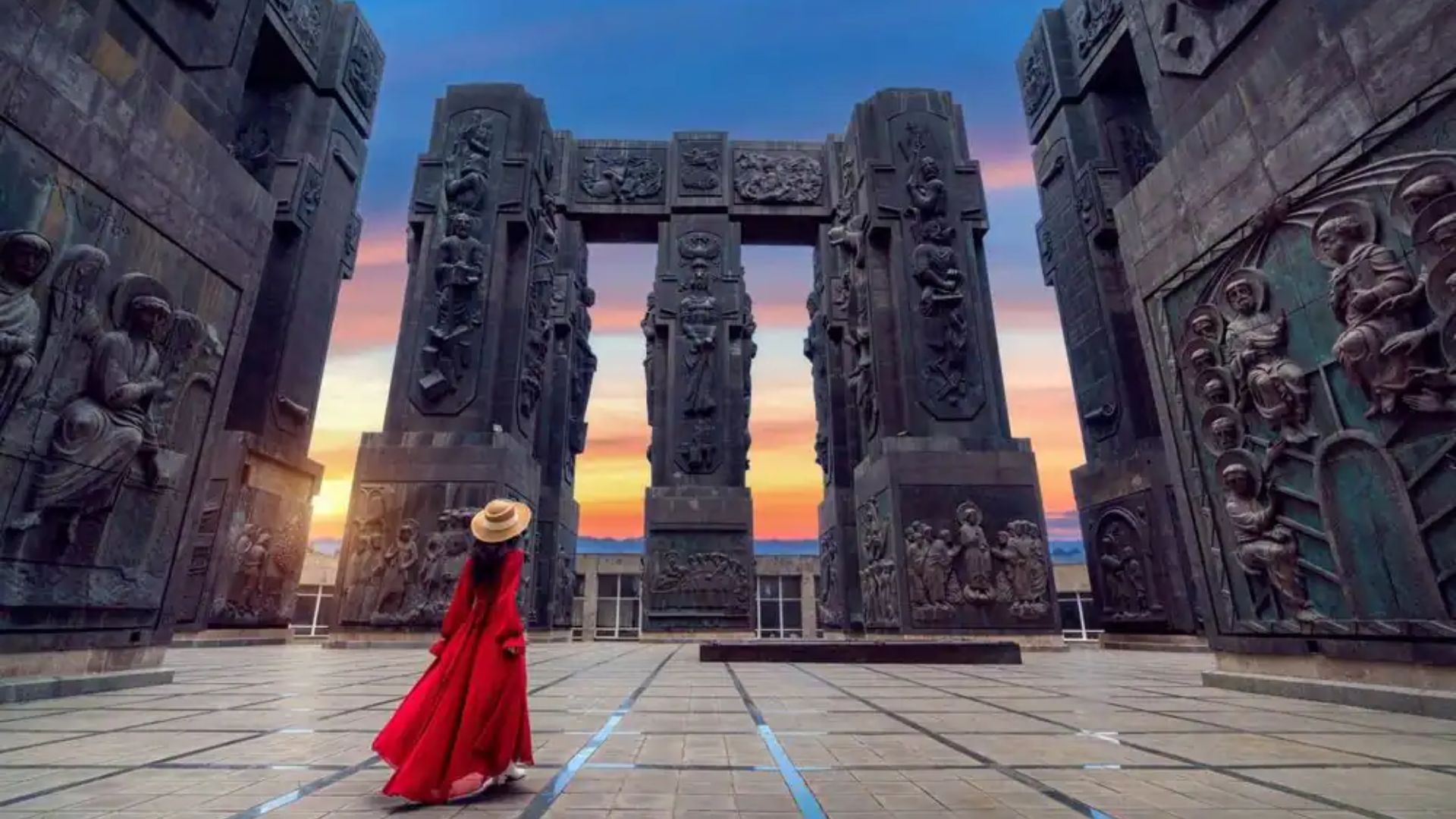 A woman in a red dress poses in front of a large monument, showcasing her elegant style against the impressive backdrop.