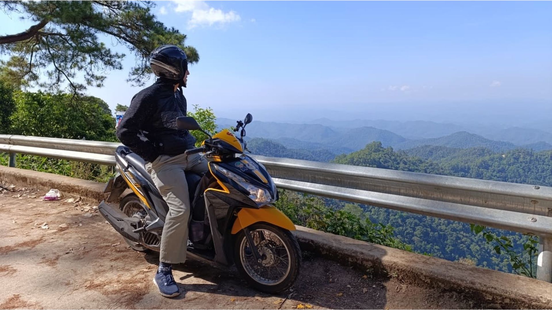 A man on a motorcycle poses against a backdrop of towering mountains, highlighting a spirit of exploration and freedom.
