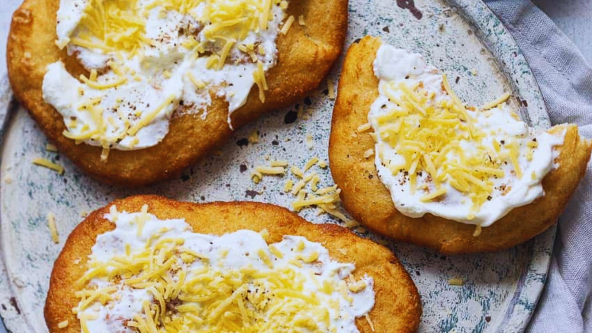 Three small baked potatoes topped with melted cheese and a dollop of sour cream on a white plate.