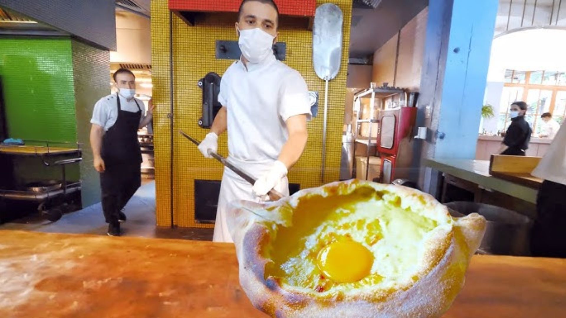 A chef cracks an egg into a bowl, preparing ingredients for a dish in a bright kitchen setting.