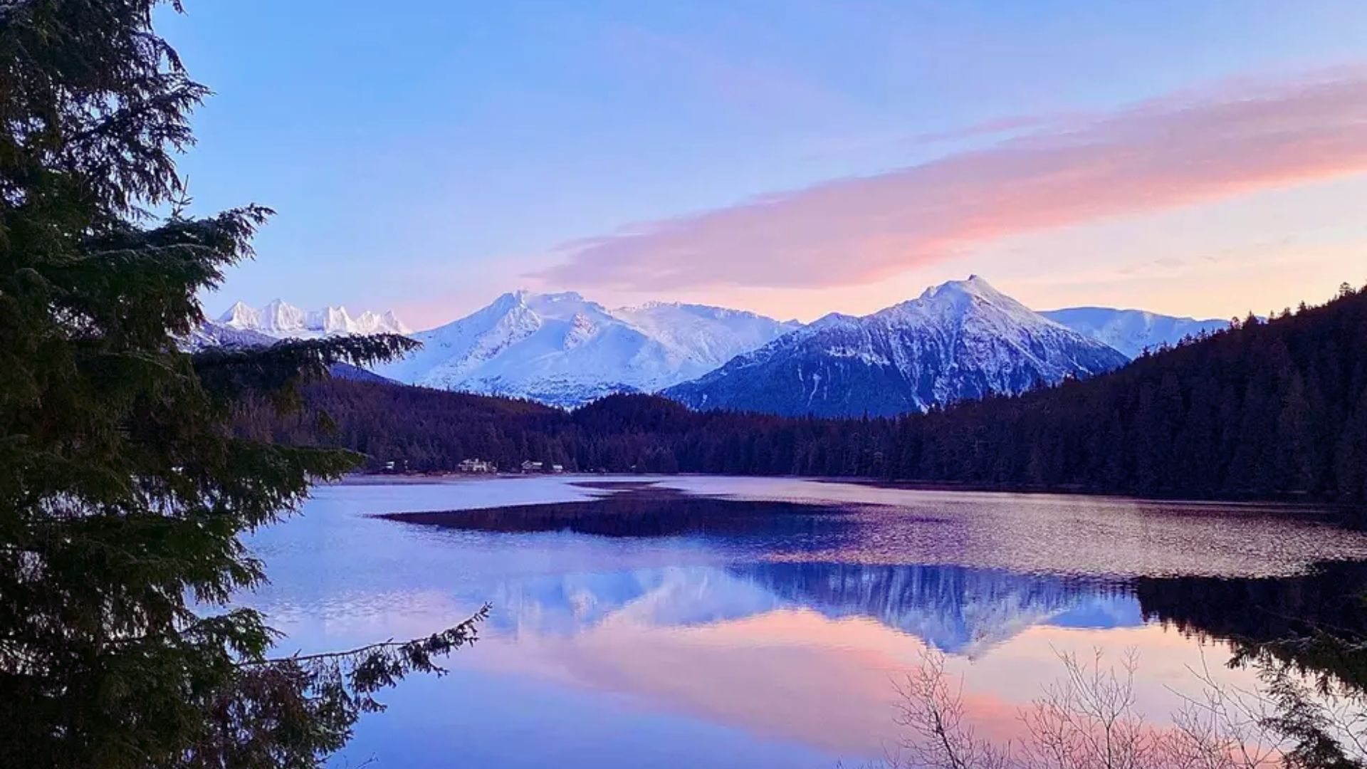 A serene lake bordered by trees and mountains, illuminated by the warm hues of a sunset.