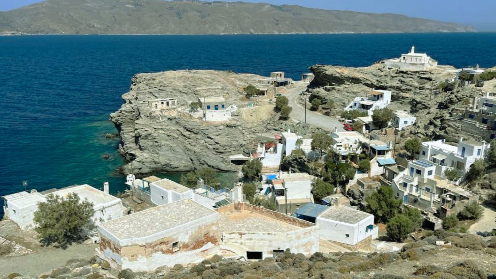 Cliffside village with whitewashed buildings and lush greenery overlooking a calm turquoise sea. The scene is serene and picturesque under a clear blue sky.