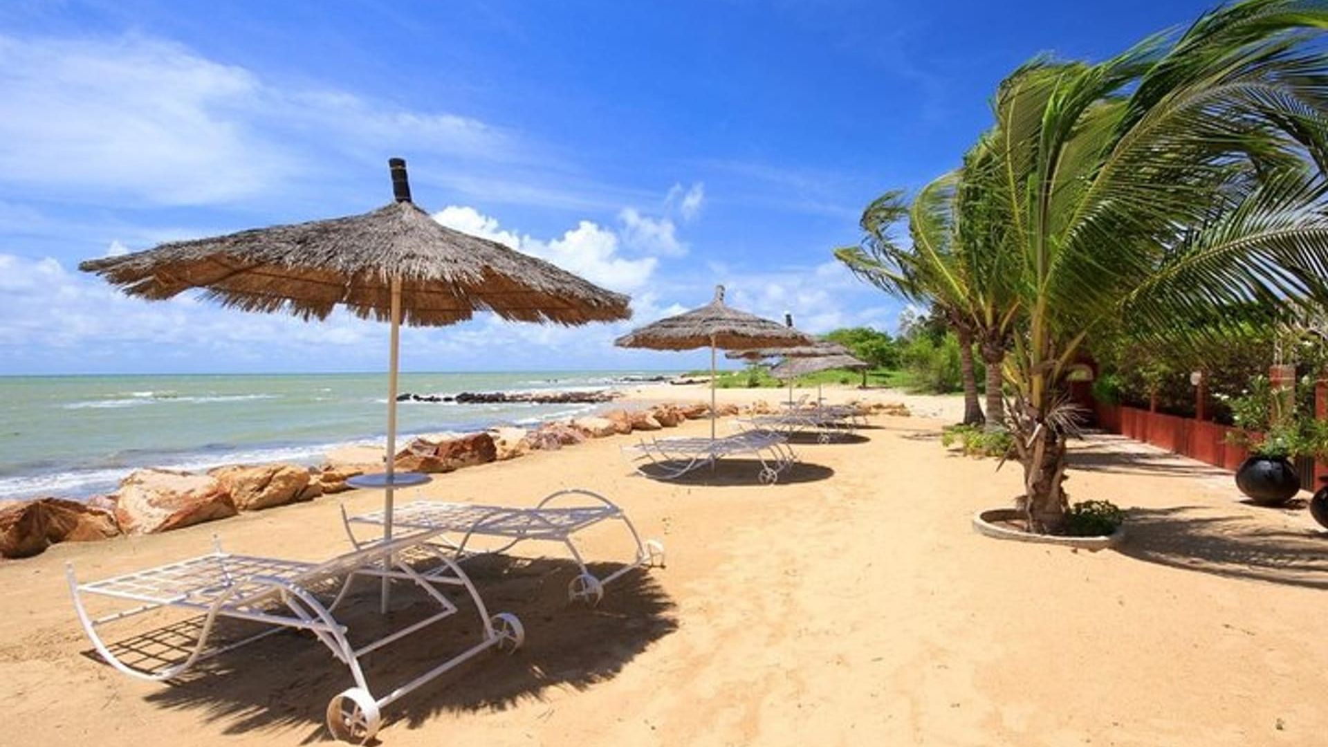Beach chairs and colorful umbrellas set up on the sandy shore, with gentle ocean waves in the background.