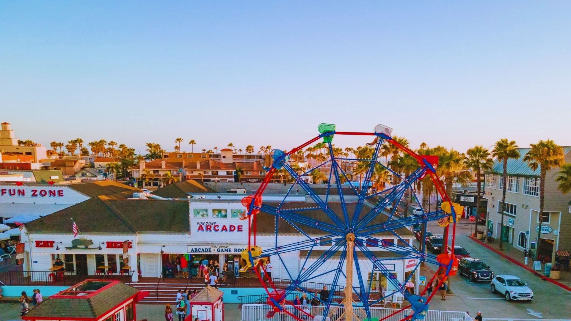 A colorful ferris wheel and amusement rides set against a sandy beach backdrop, with clear blue skies above.