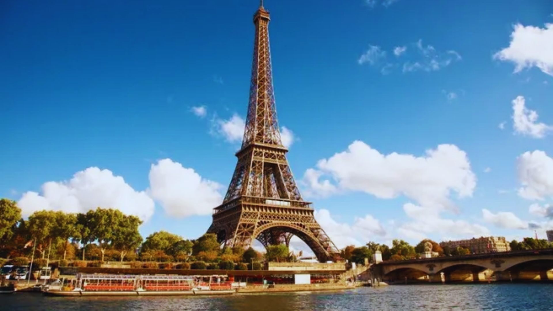 The Eiffel Tower rises majestically above the water, framed by a clear blue sky and gentle ripples below.