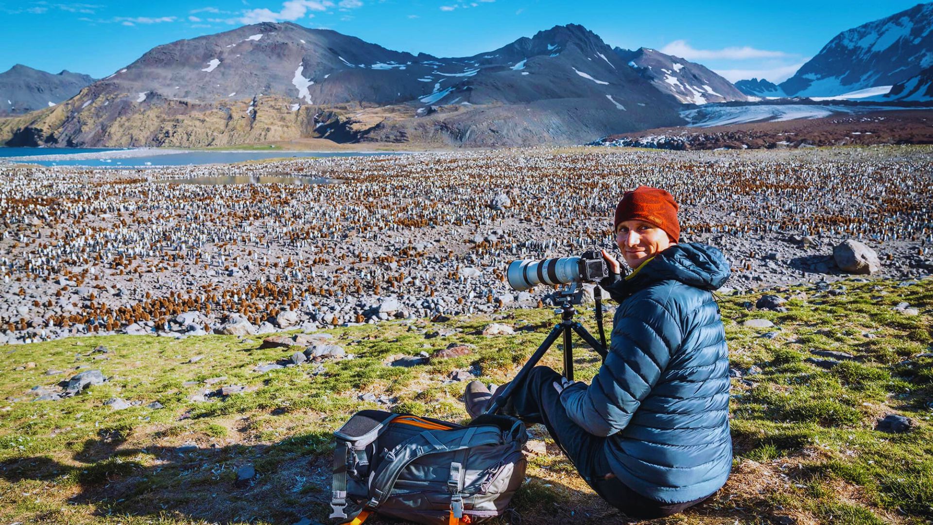 A woman taking a picture of a majestic mountain range in the background.