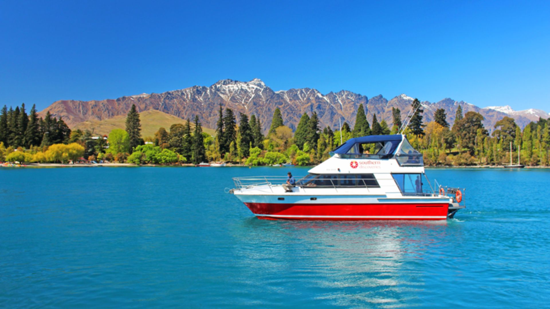 A boat floats on a serene lake, with majestic mountains rising in the background under a clear blue sky.