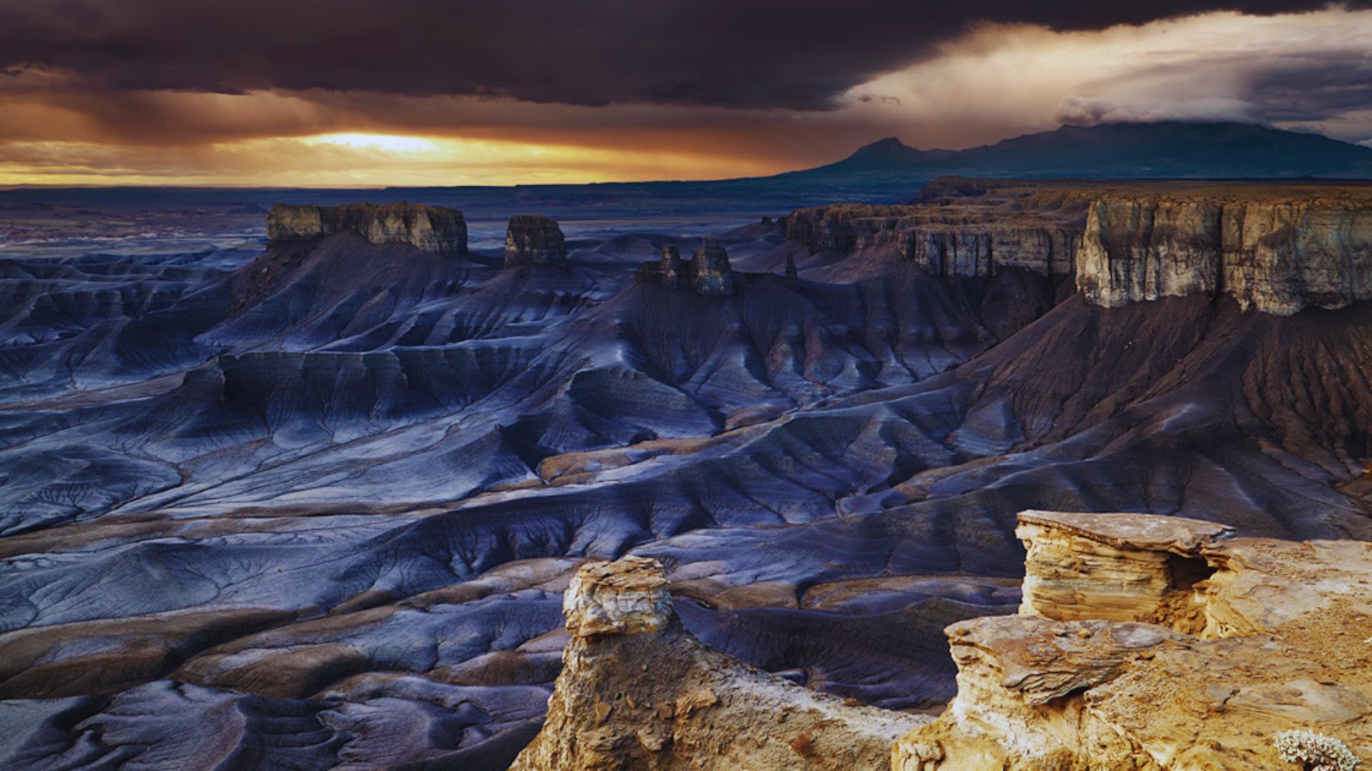 The sun sets, casting warm hues over the desert landscape and distant mountains.