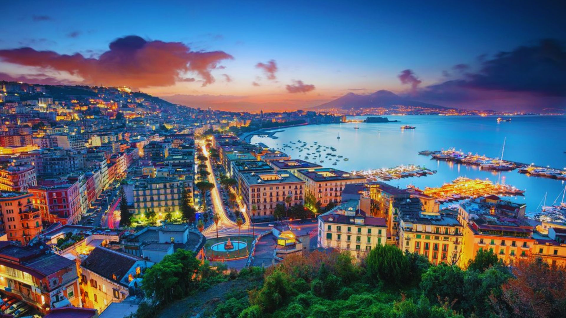 Naples, Italy at dusk, showcasing a skyline illuminated by city lights against a twilight sky.