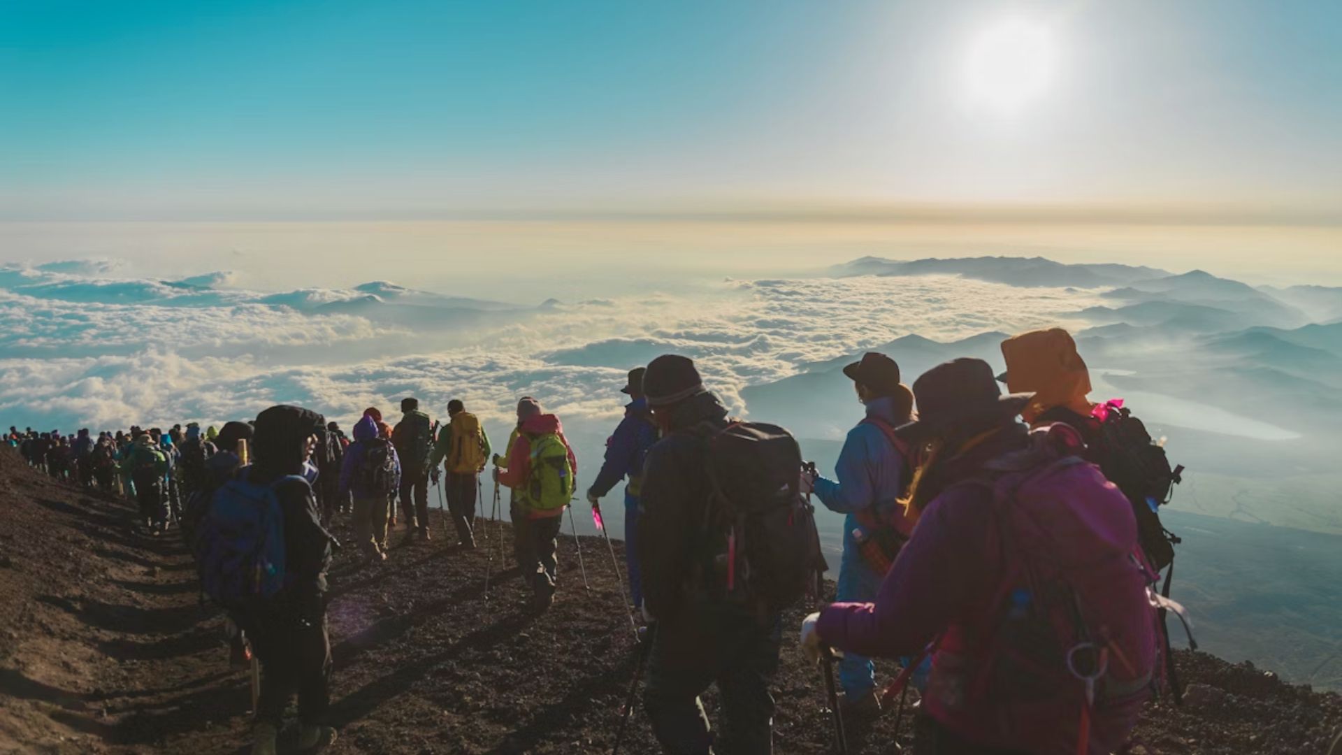 A group of hikers ascends a mountainside at sunrise, surrounded by a sea of clouds. The scene conveys adventure and awe in a serene atmosphere.