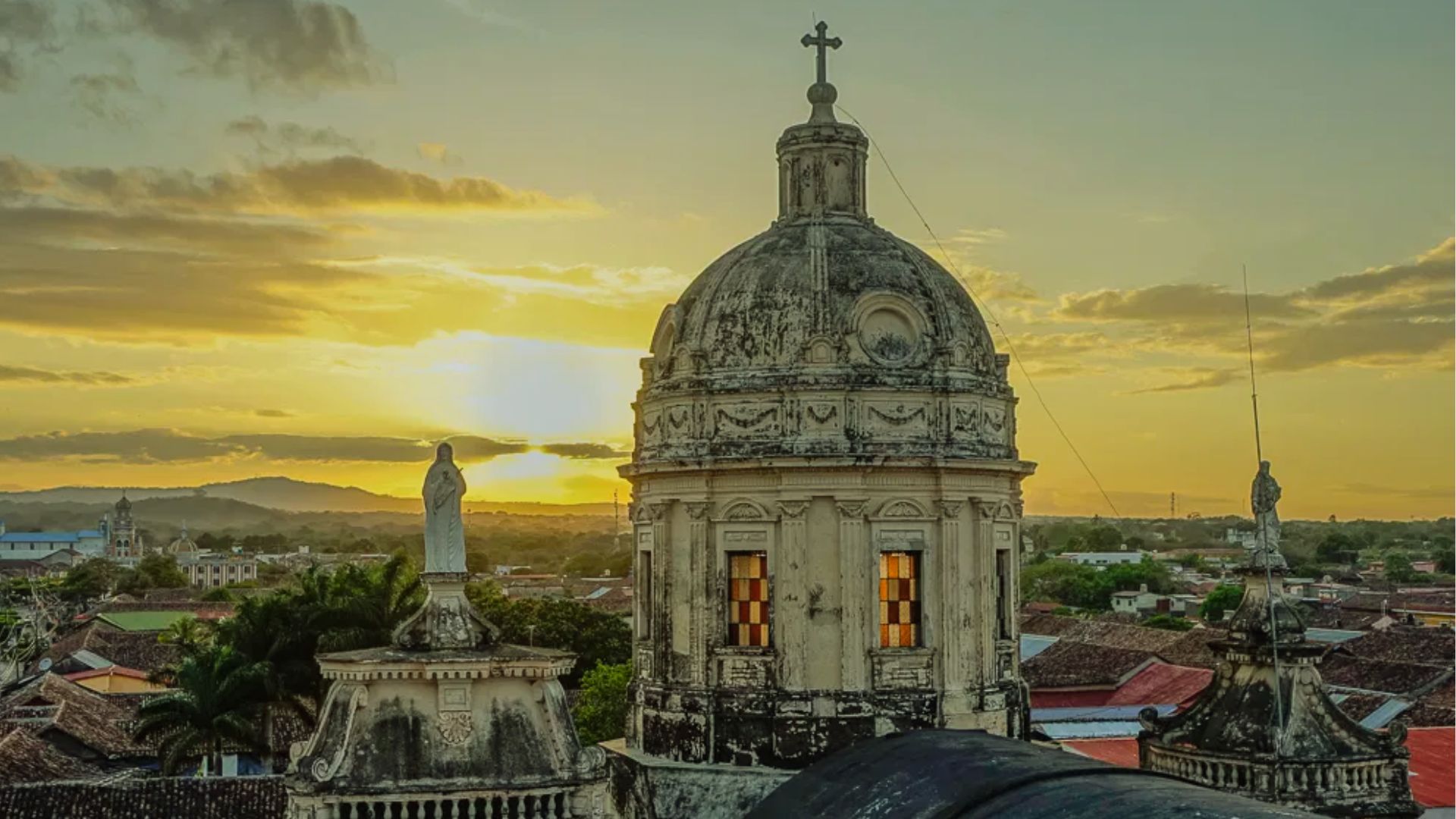 Sunset view of a historic cityscape featuring an ornate church dome with a cross. Warm light bathes the scene, creating a tranquil atmosphere.