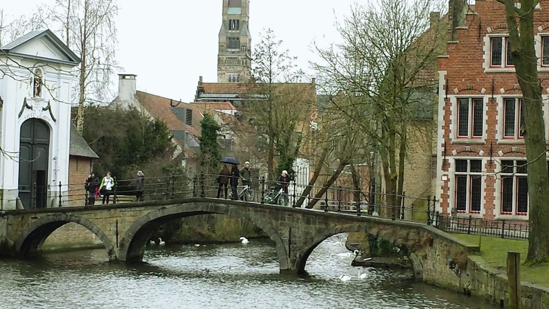 A quaint bridge spans a canal in a small town, surrounded by charming buildings and greenery.
