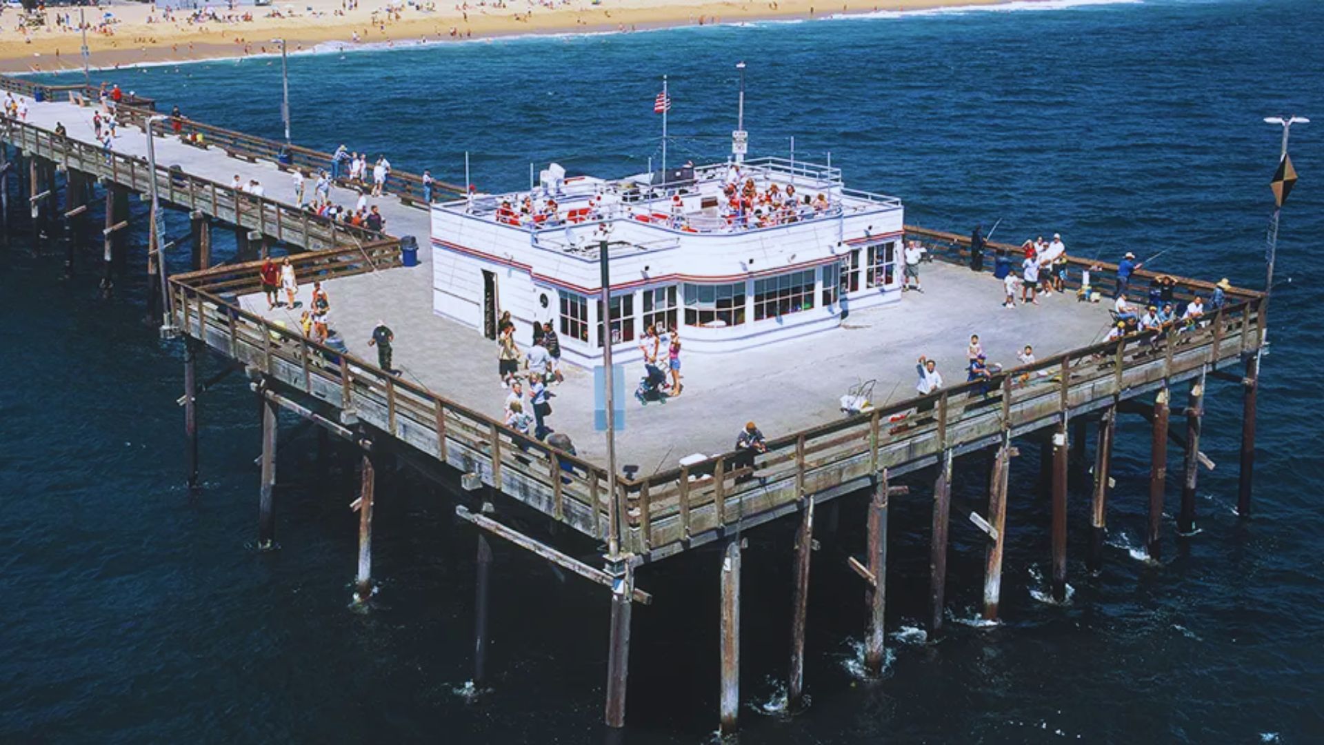 A crowded pier with people walking and relaxing, highlighted by a restaurant at the end, overlooking the water.