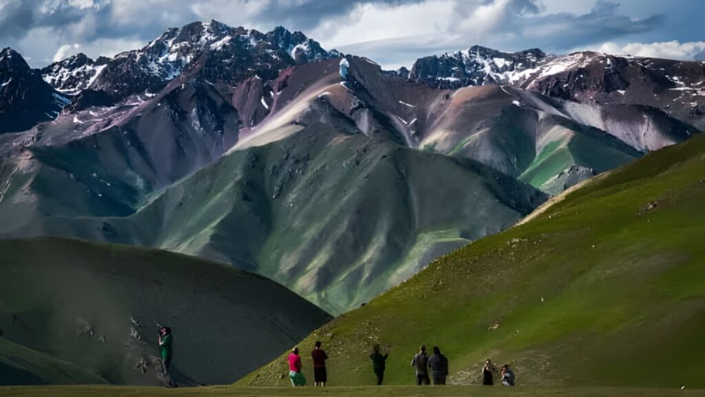 A group of people stands on a hill, gazing at a scenic mountain range in the distance.