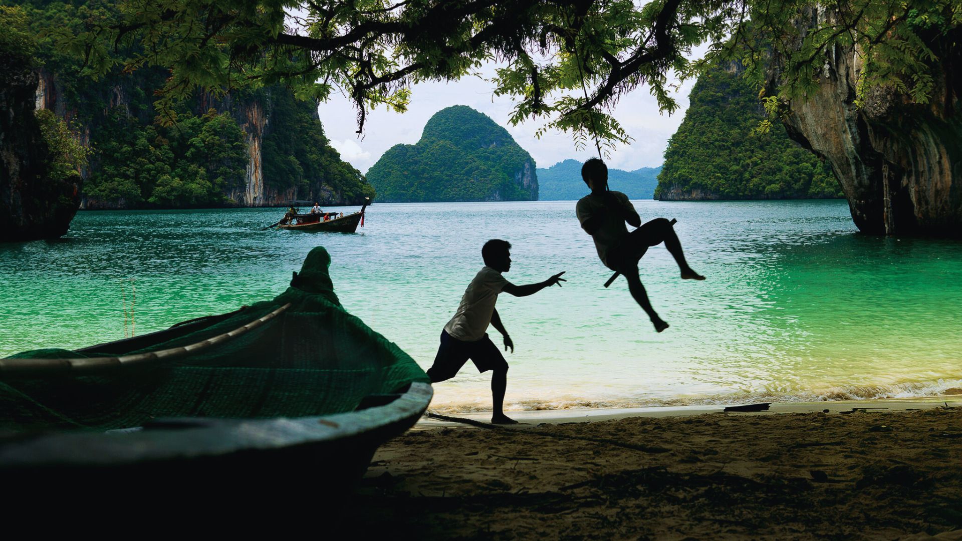Two boys joyfully jumping into the water beside a small boat on a sunny day.