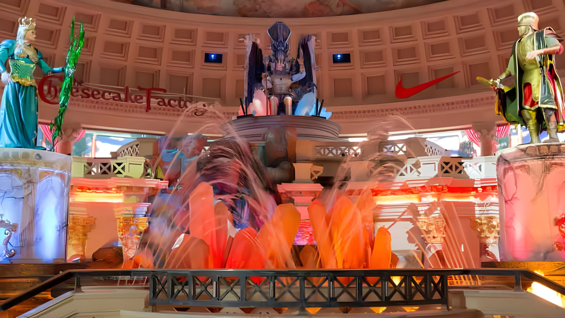 Illuminated fountains surrounded by statues of people create a vibrant nighttime scene.