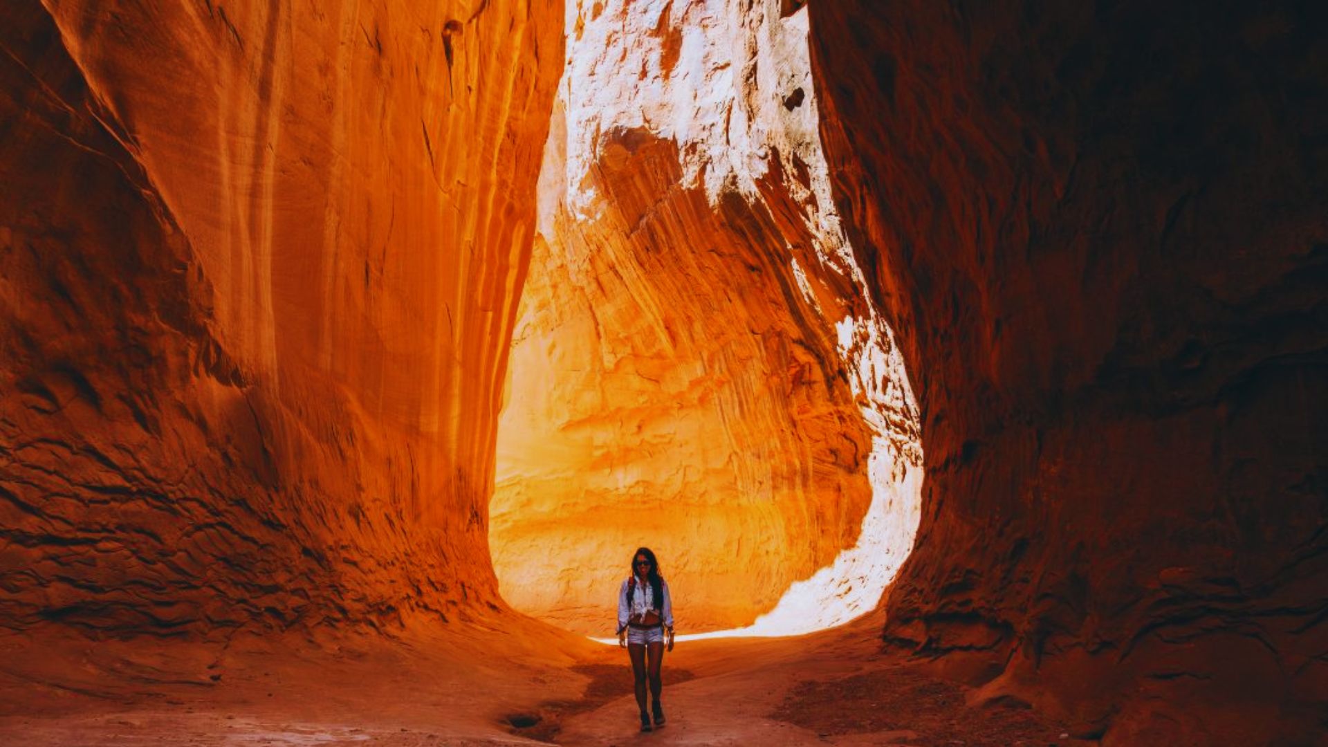 A woman navigating a narrow canyon, with high rock walls on either side and sunlight casting shadows on the ground.